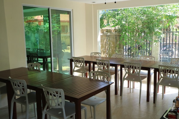 Un comedor con una mesa de madera y sillas blancas, ventanas amplias con vistas a follaje, y un divisor corredizo que da a un patio exterior.