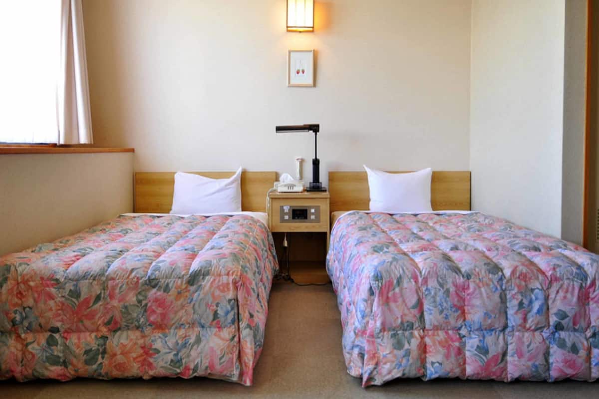 Ein Hotelzimmer mit zwei Einzelbetten, jeweils mit floralem Bettbezug, einem Nachttisch mit Lampe, einem kleinen Bilderrahmen und einem Nachtschränkchen.