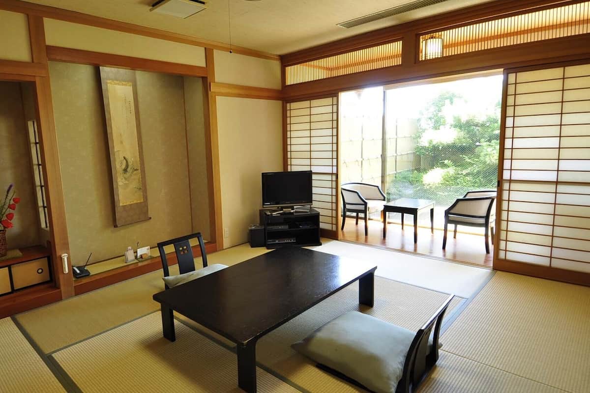 Une pièce de style japonais traditionnel, avec un sol recouvert de tatamis, une table basse, des chaises, un téléviseur et des portes coulissantes donnant sur un balcon.