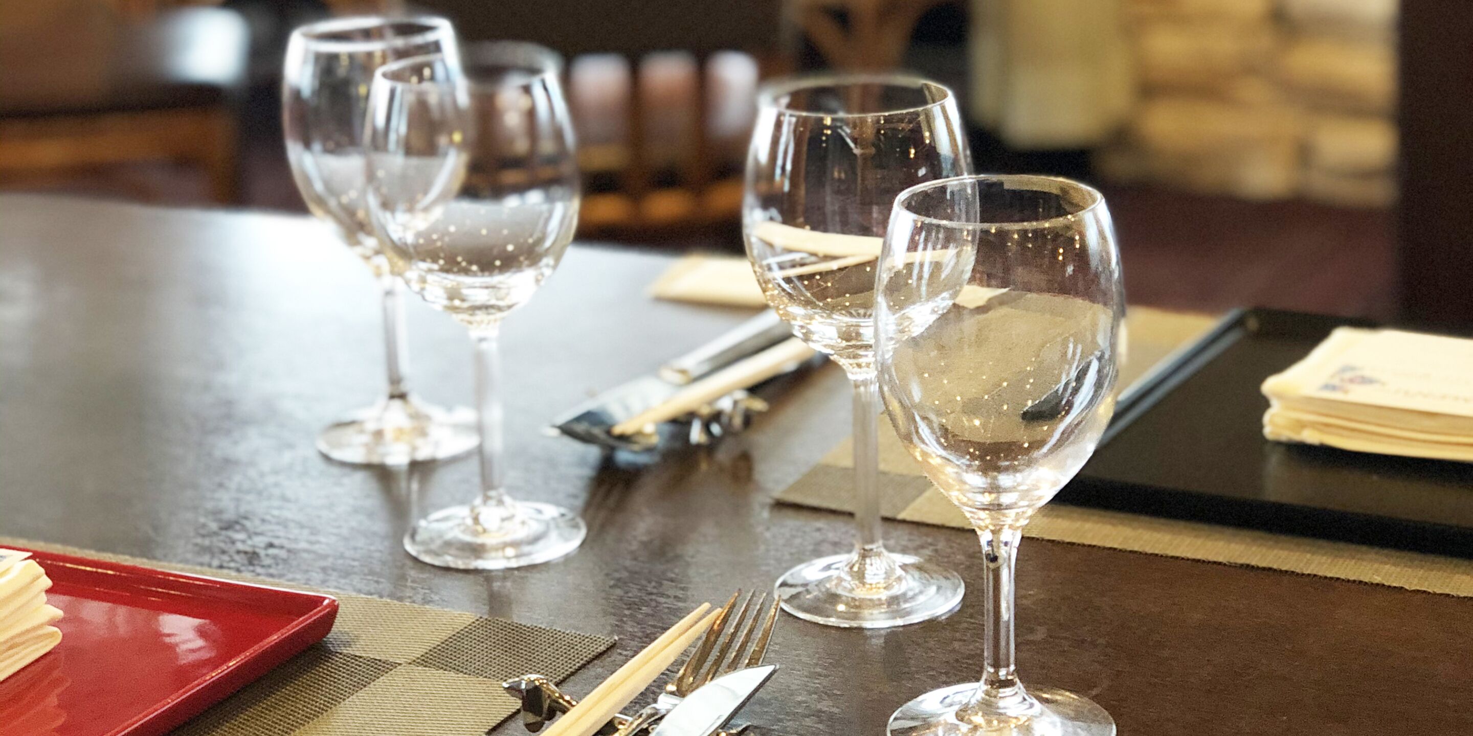 Una mesa servida con copas de vino, cubiertos y una bandeja roja.