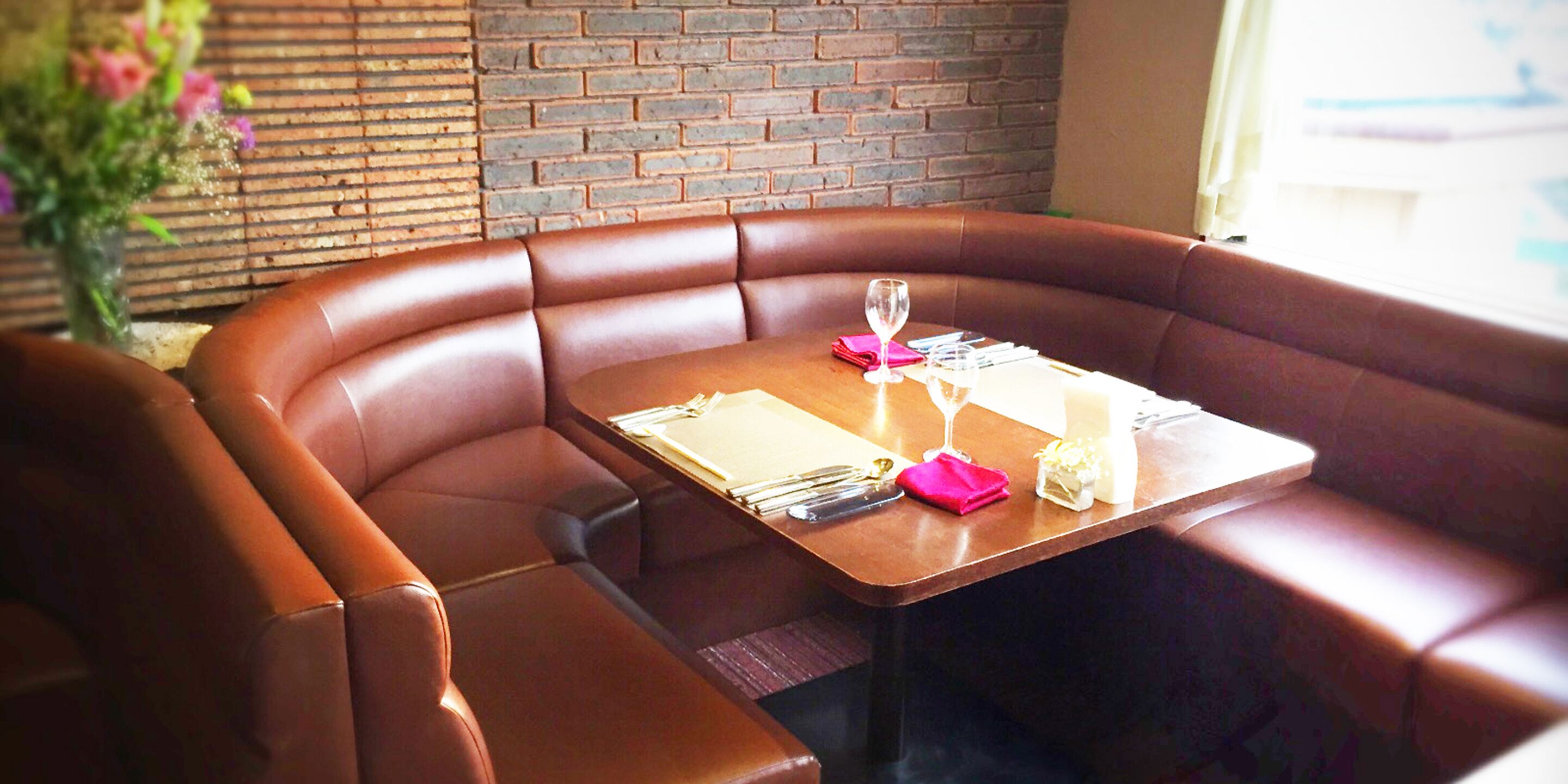 A restaurant booth with a wooden table set for two, including cutlery and a glass.