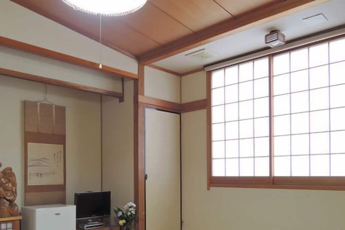 Une pièce de style japonais traditionnel, avec un sol recouvert de tatamis, une table basse, un téléviseur et une porte coulissante.