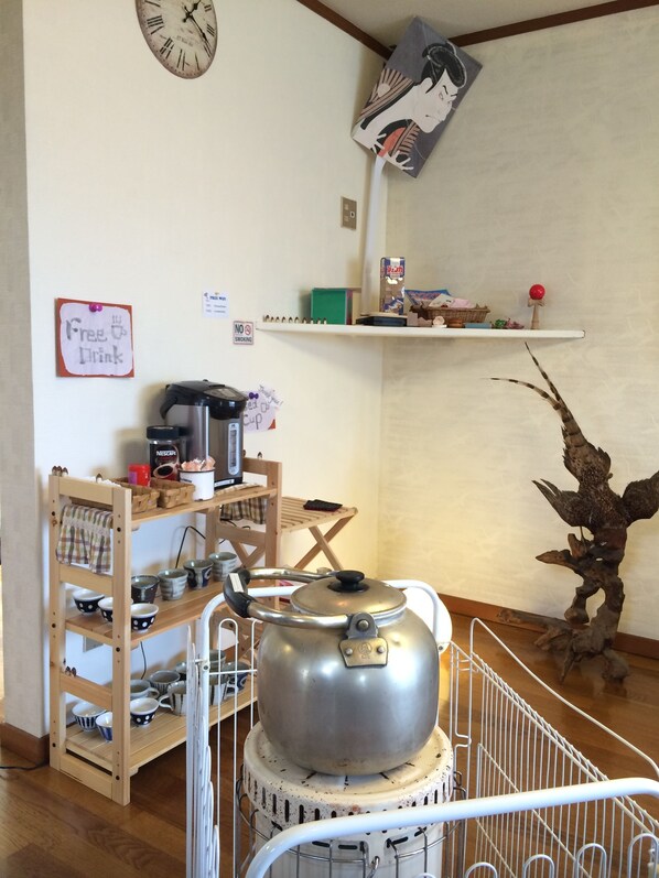 A kitchen with a kettle on a stand, a shelf with various items, and a wall clock. - Nozawa Dream (Nozawaonsen)