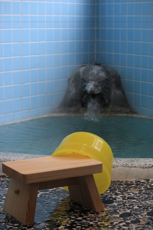 A small wooden stool in front of a pool with a water feature in the background.