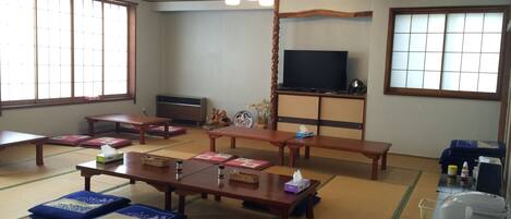 Una habitación tradicional japonesa con esteras de tatami, mesas bajas y un televisor sobre un mueble.