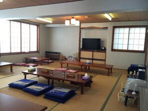 A traditional Japanese-style room with tatami mats, low tables, and a television on a cabinet. - Nozawa Dream (Nozawaonsen)