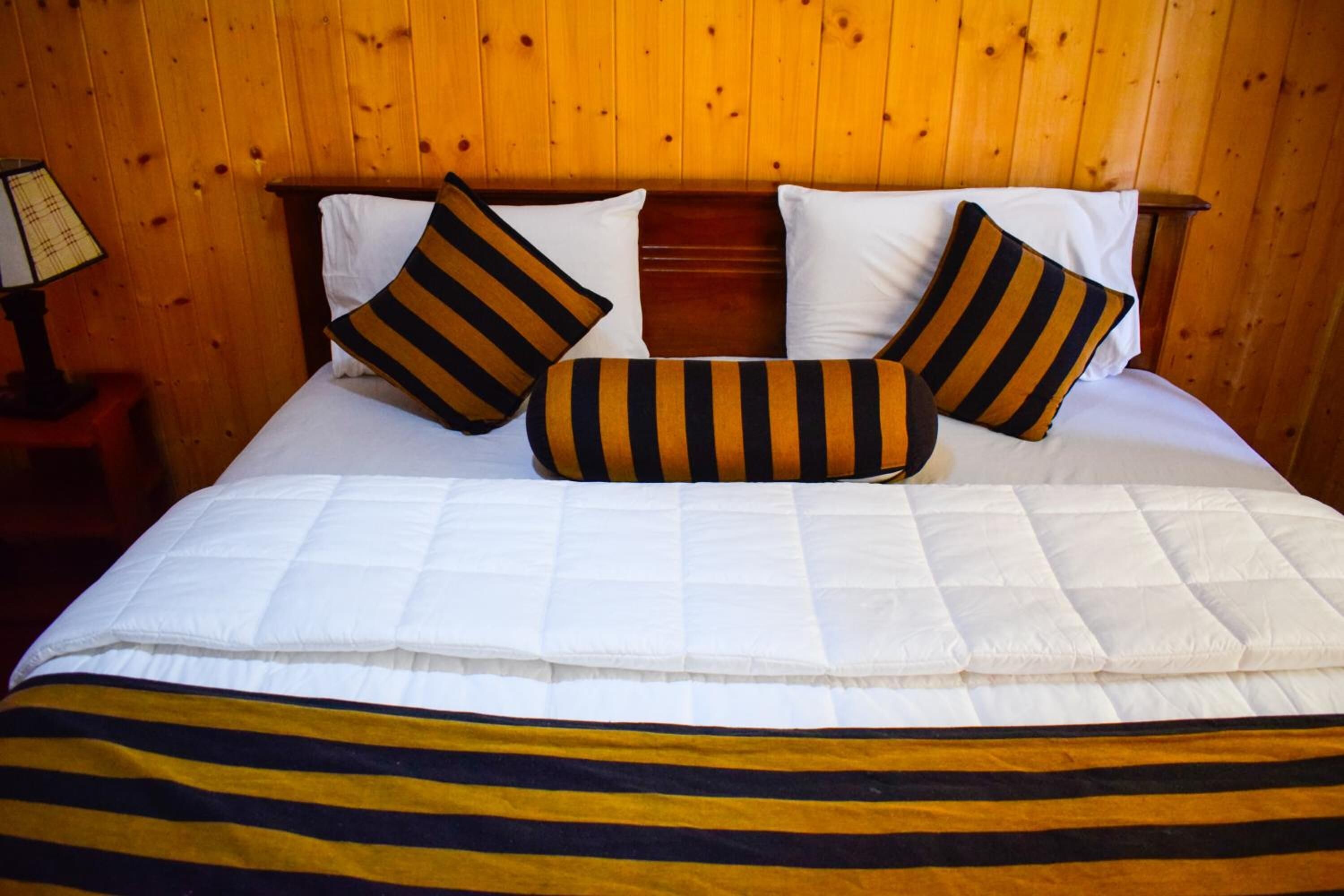 A neatly made bed with white bedding and striped pillows, set against a wooden paneled wall.