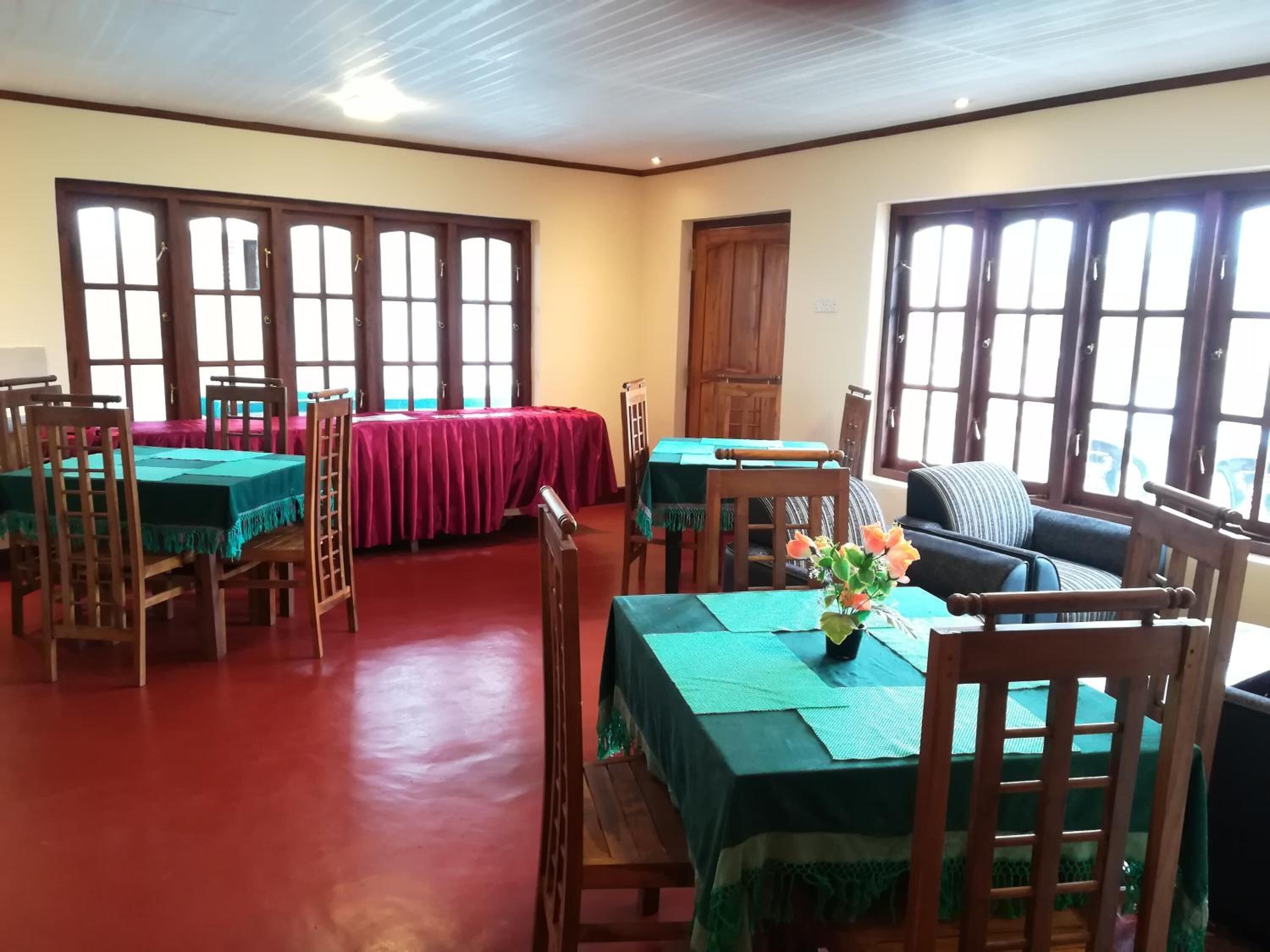 A dining area with wooden tables and chairs, a sofa, and large windows with curtains.