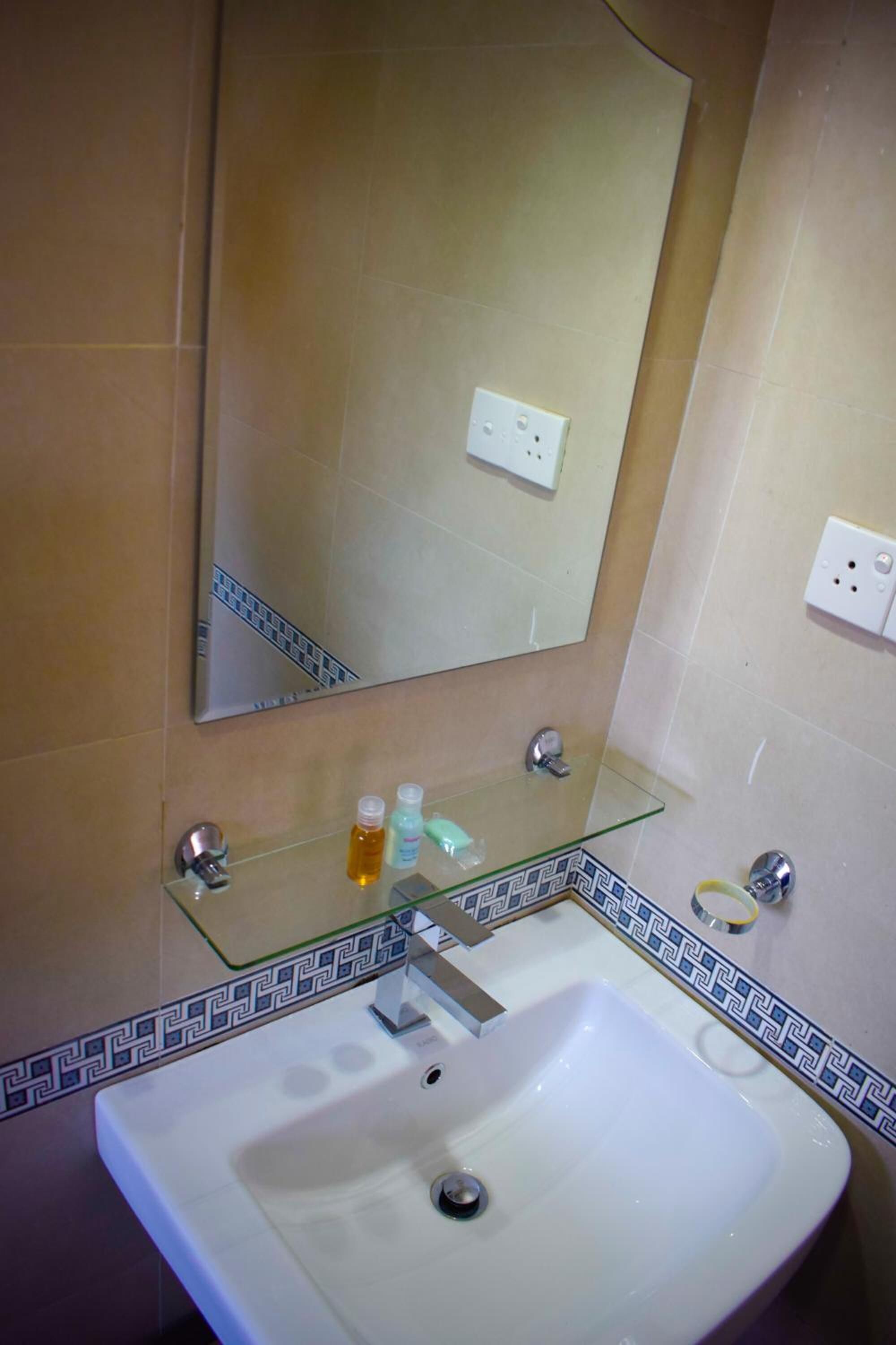 Un baño con un lavamanos blanco, un estante de vidrio con artículos de tocador, un espejo y un salpicadero de azulejos estampados.
