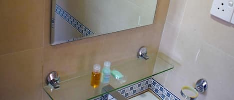 Un baño con un lavamanos blanco, un estante de vidrio con artículos de tocador, un espejo y un salpicadero de azulejos estampados.