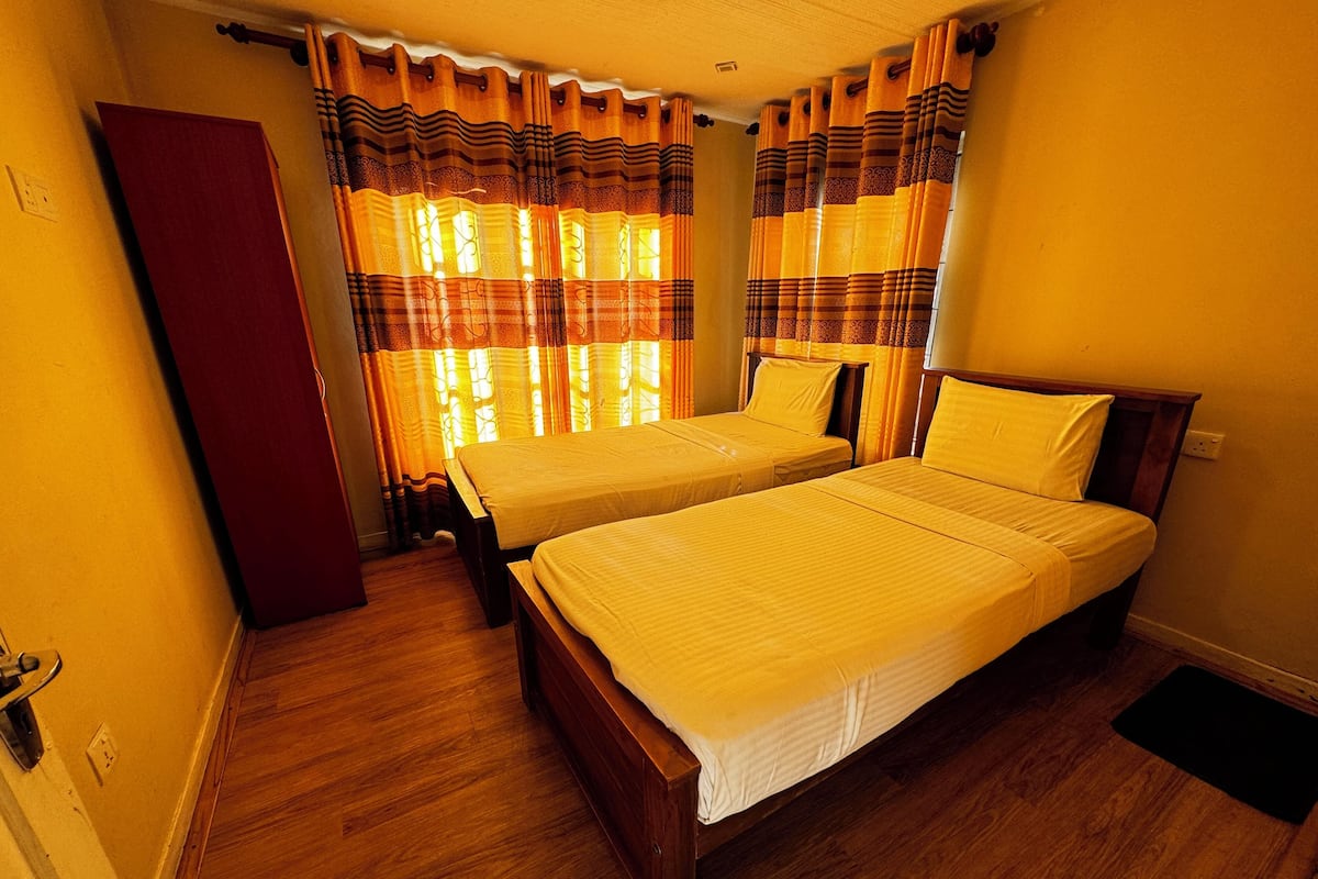 A room with two beds, wooden flooring, and curtains with a striped pattern.