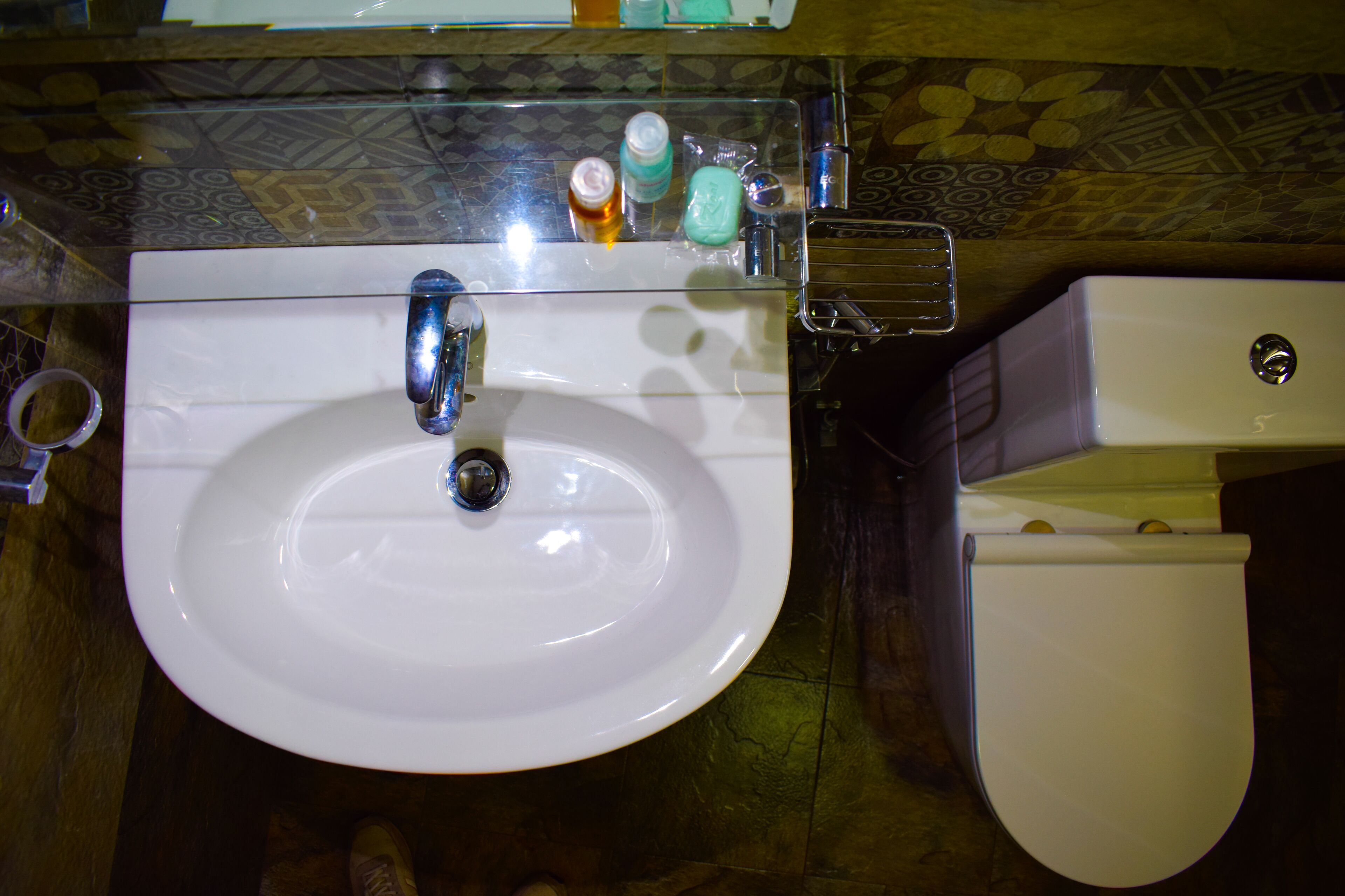 Un baño con un lavabo blanco, un espejo encima y artículos de aseo sobre el borde del lavabo.
