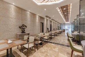 Un amplio vestíbulo de hotel con varias mesas y sillas de comedor, un techo alto con vigas de madera y una pared con textura.