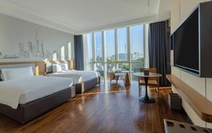 Habitación de hotel con dos camas, un balcón, televisión y vistas panorámicas de la ciudad.