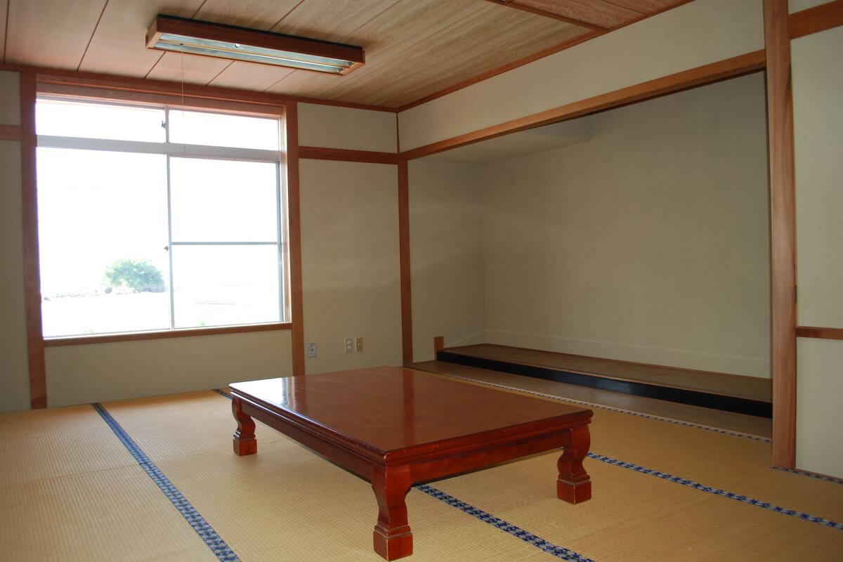A room with tatami flooring, a wooden table, a large window, and a sliding door.