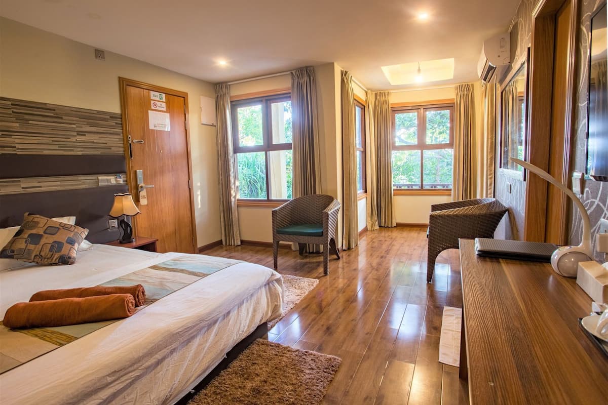 Une chambre d’hôtel avec un lit, deux chaises, un bureau et de grandes fenêtres.