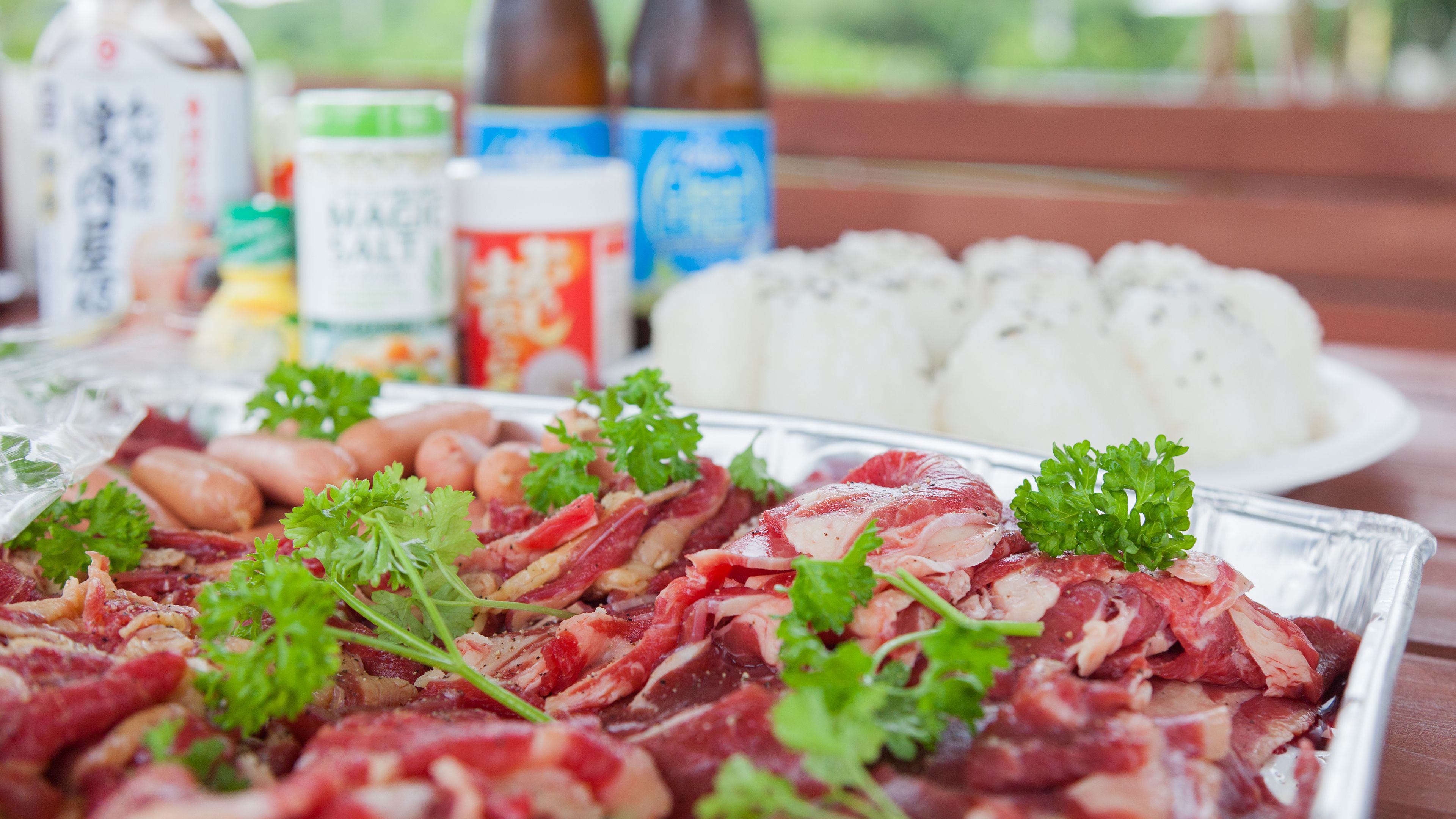 A table with raw meat, vegetables, and condiments.
