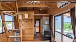 A cabin with wooden walls, a loft bed, a kitchenette, and large windows offering a view of the outdoors. - Motobu Ikoi no Yado Yamachan (Motobu)