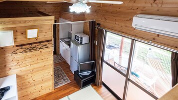 Cocina compacta con microondas, refrigerador y una pequeña televisión. Cuenta con un ventilador de techo de madera, una ventana con vistas al exterior y una puerta que da a un balcón.