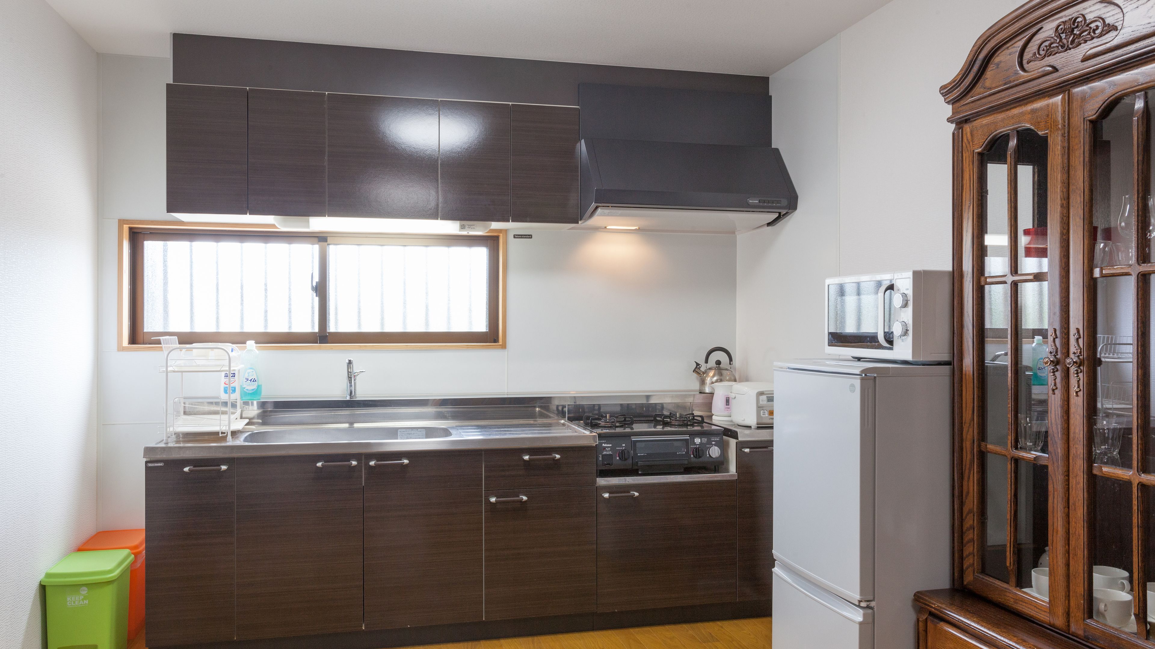 Una cocina con armarios de madera oscura, un lavamanos de acero inoxidable, un microondas y una estufa.