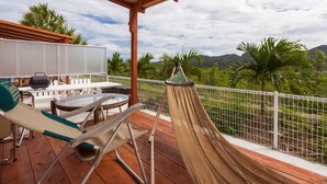 A wooden deck with a hammock, outdoor furniture, and a view of mountains and palm trees. - Motobu Ikoi no Yado Yamachan (Motobu)