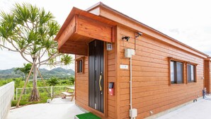 A wooden cabin with a black door, a small window, and a balcony with a table and chairs. - Motobu Ikoi no Yado Yamachan (Motobu)