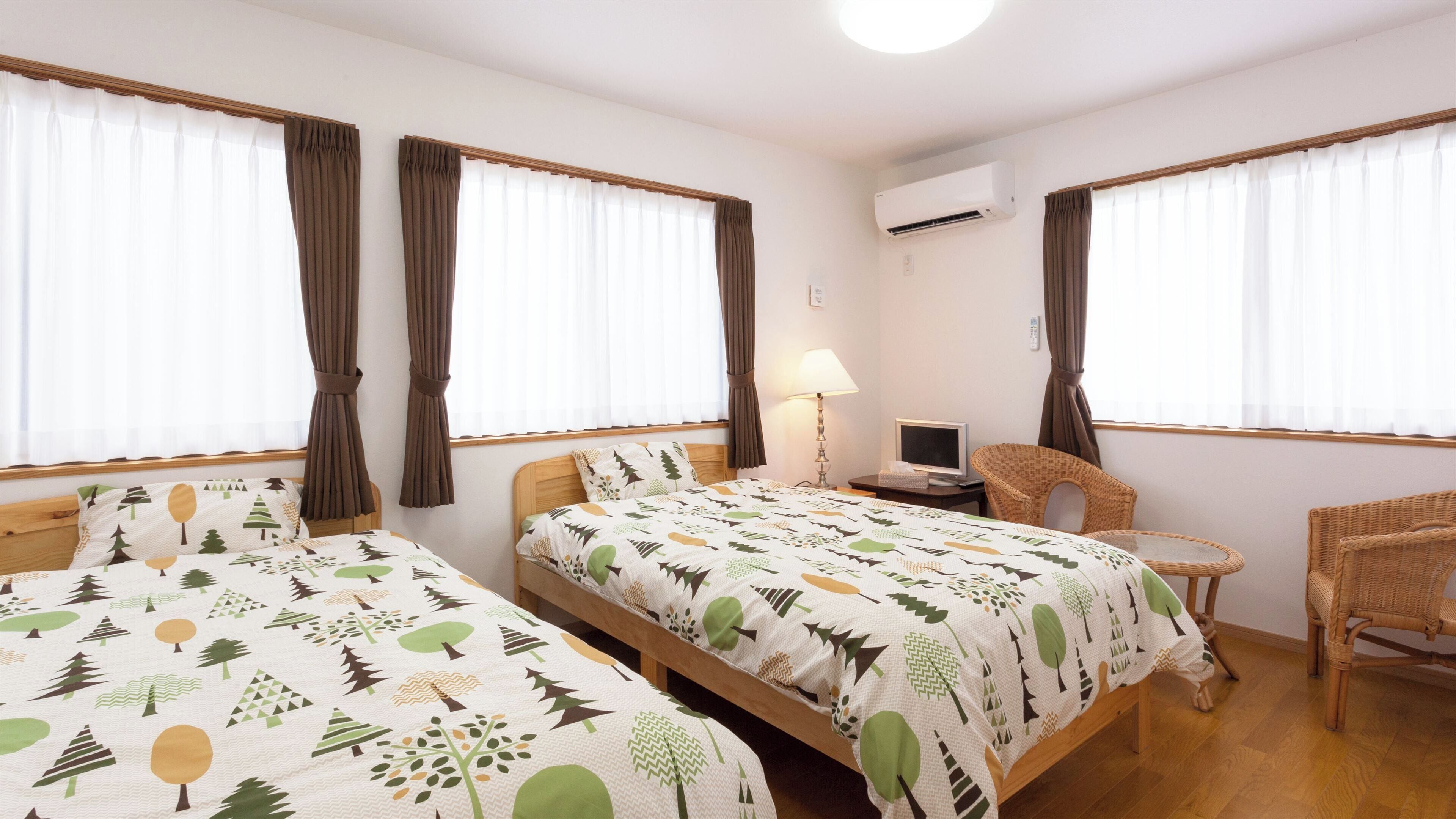 A hotel room with two beds, a desk with a computer, a chair, and an air conditioning unit.