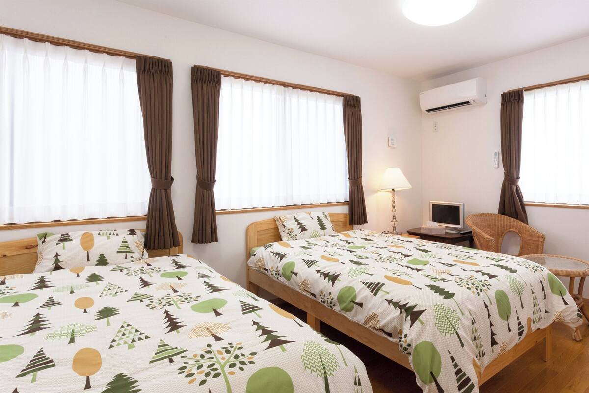 A hotel room with two beds, a desk with a computer, a chair, and an air conditioning unit.