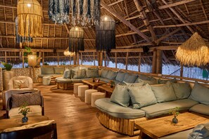 A spacious lounge area with a thatched roof, wooden furniture, and hanging light fixtures. - Kendwa Rocks Beach Hotel (Kendwa)