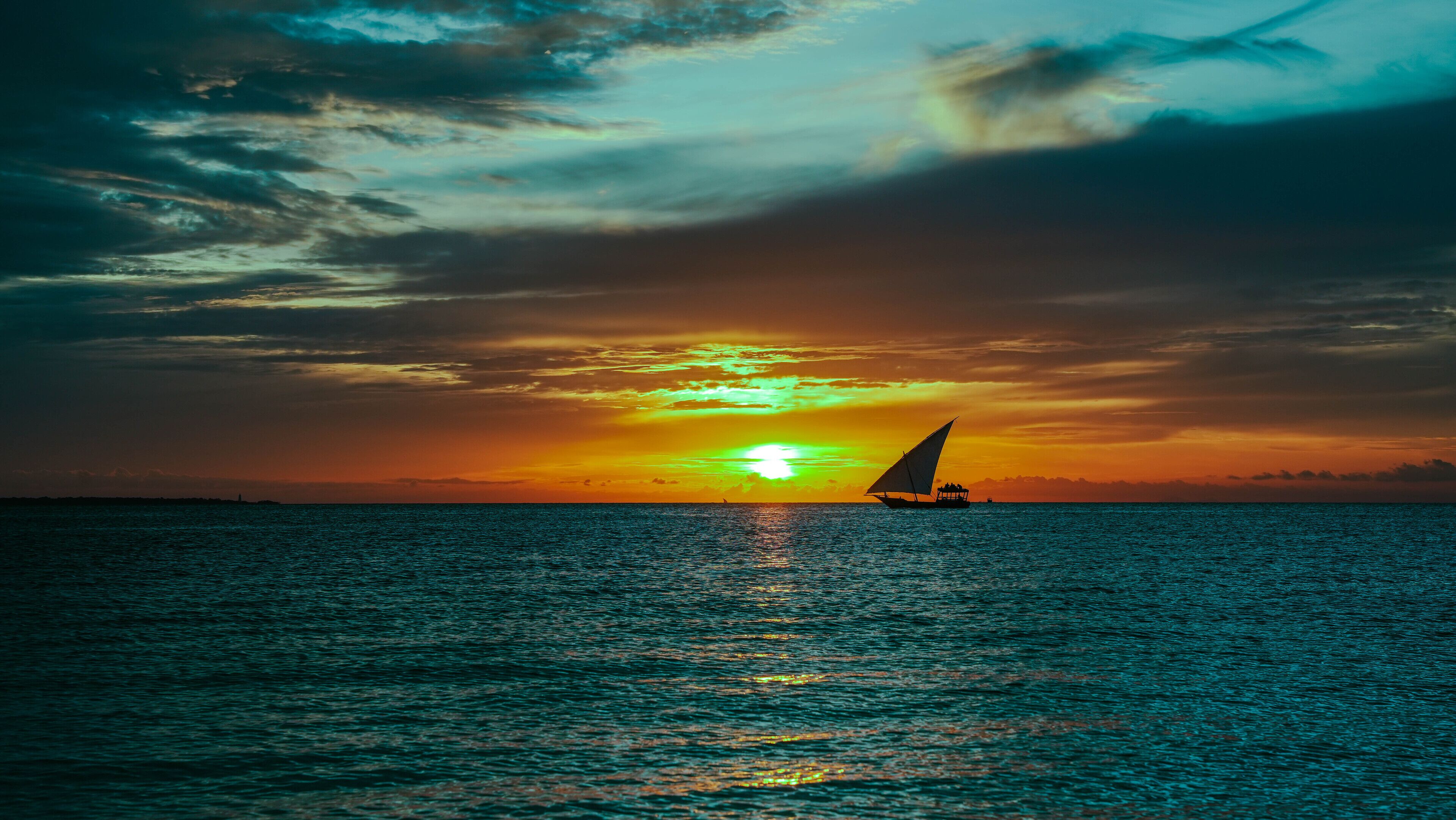 A sunset over the ocean with a sailboat.