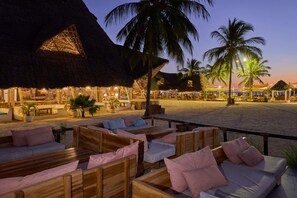 A beachside lounge with wooden furniture and thatched-roof structures.