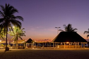 A beachside resort with thatched-roof huts, palm trees, and string lights. - Kendwa Rocks Beach Hotel (Kendwa)
