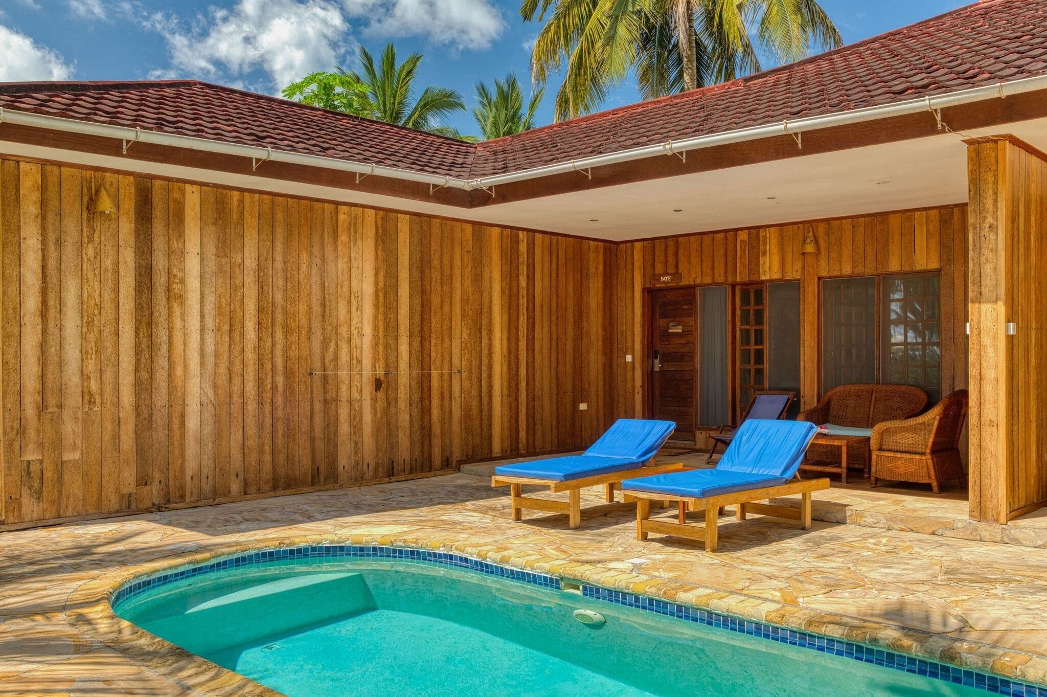 A wooden villa with a swimming pool, two lounge chairs, and a covered patio area.