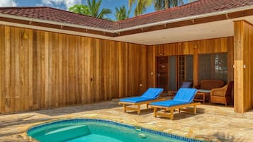 A wooden villa with a swimming pool, two lounge chairs, and a covered patio area.