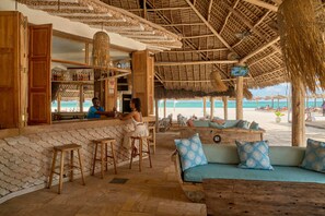 A beachside bar with wooden furniture and a thatched roof.