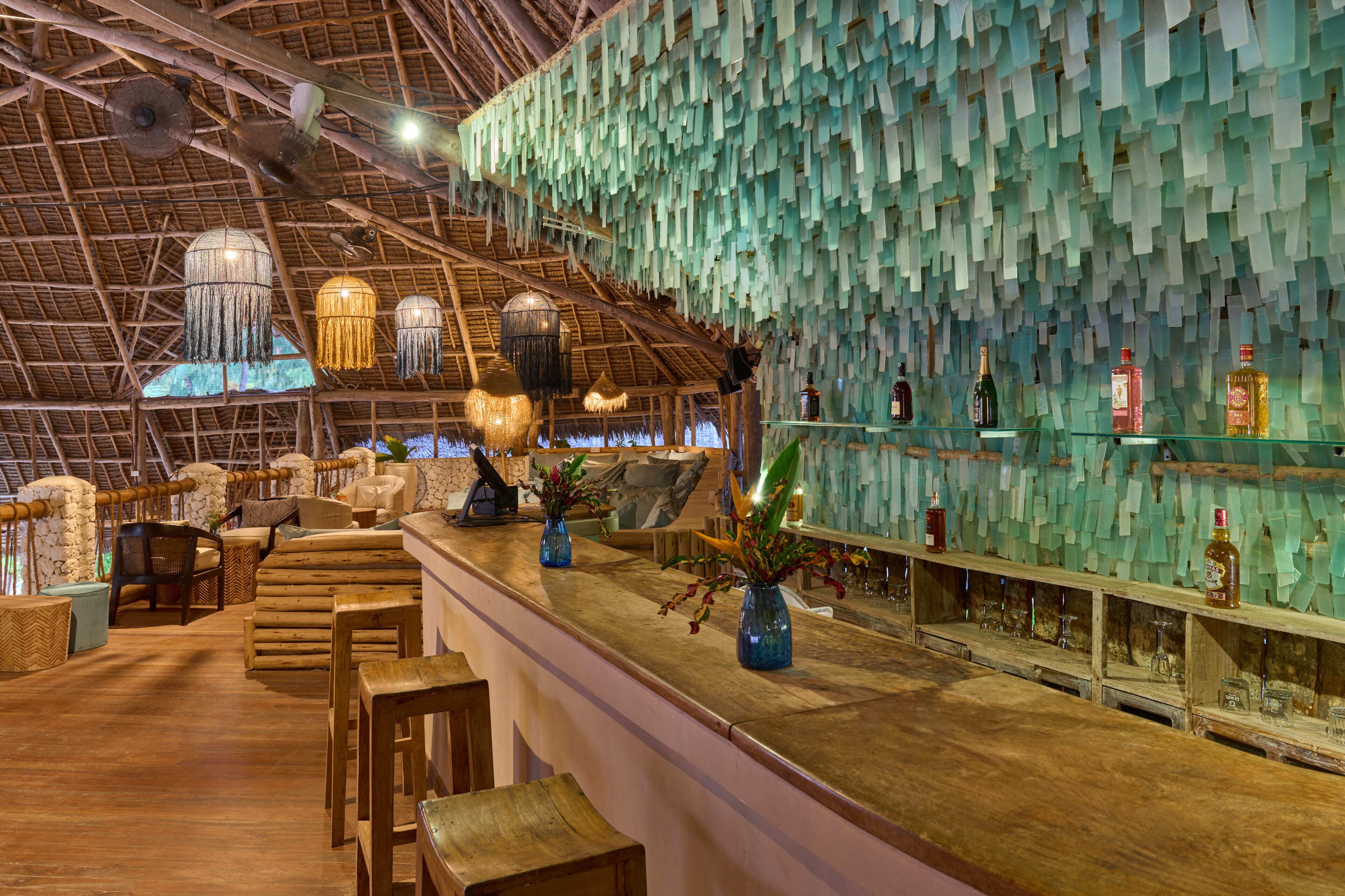 A bar area with a wooden counter, hanging lights, and a wall decorated with paper strips.