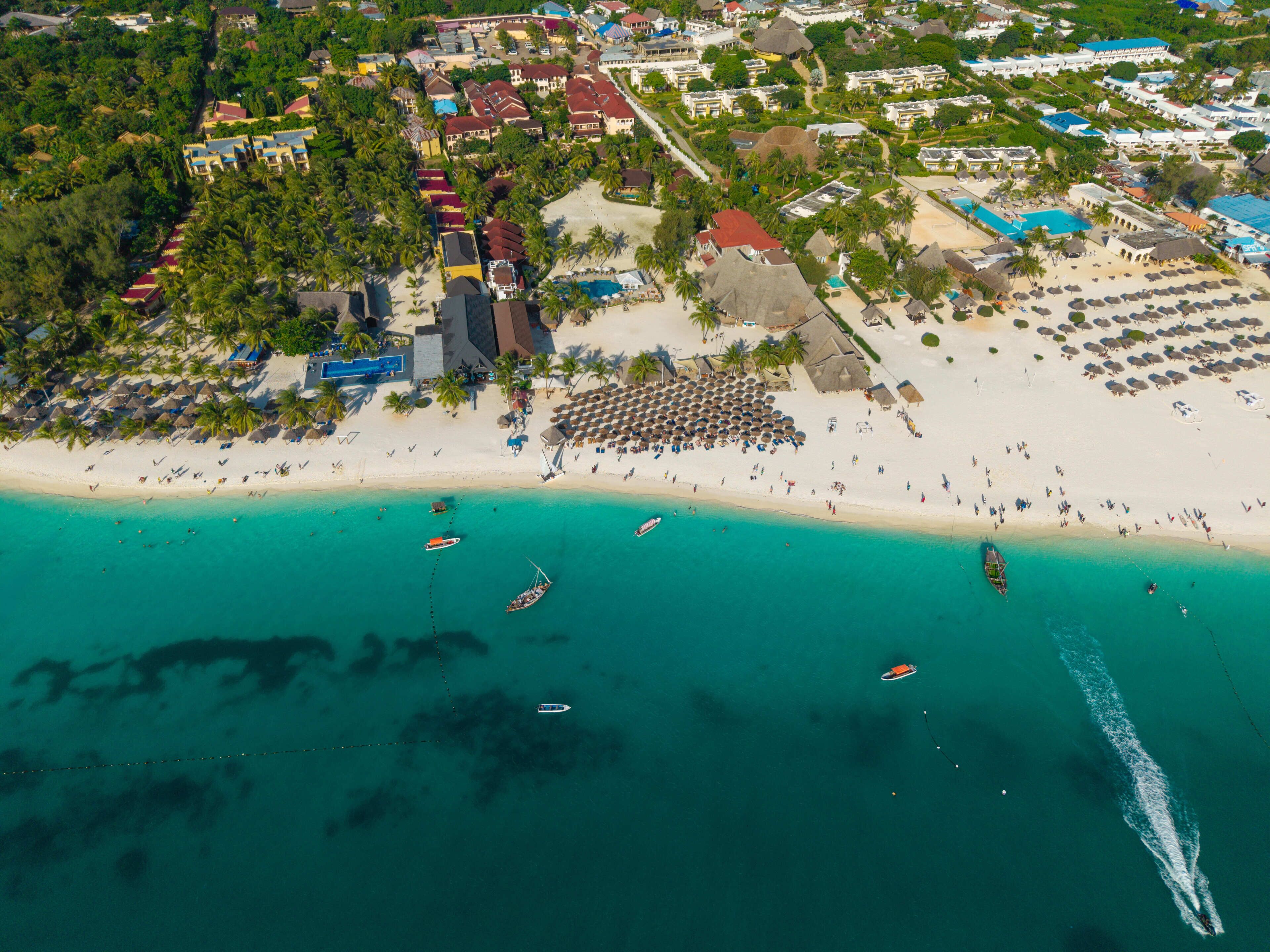 An aerial view of a coastal resort with beachfront villas, a sandy beach, and boats in the water.