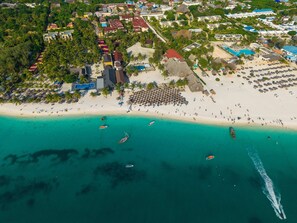 An aerial view of a coastal resort with beachfront villas, a sandy beach, and boats in the water.