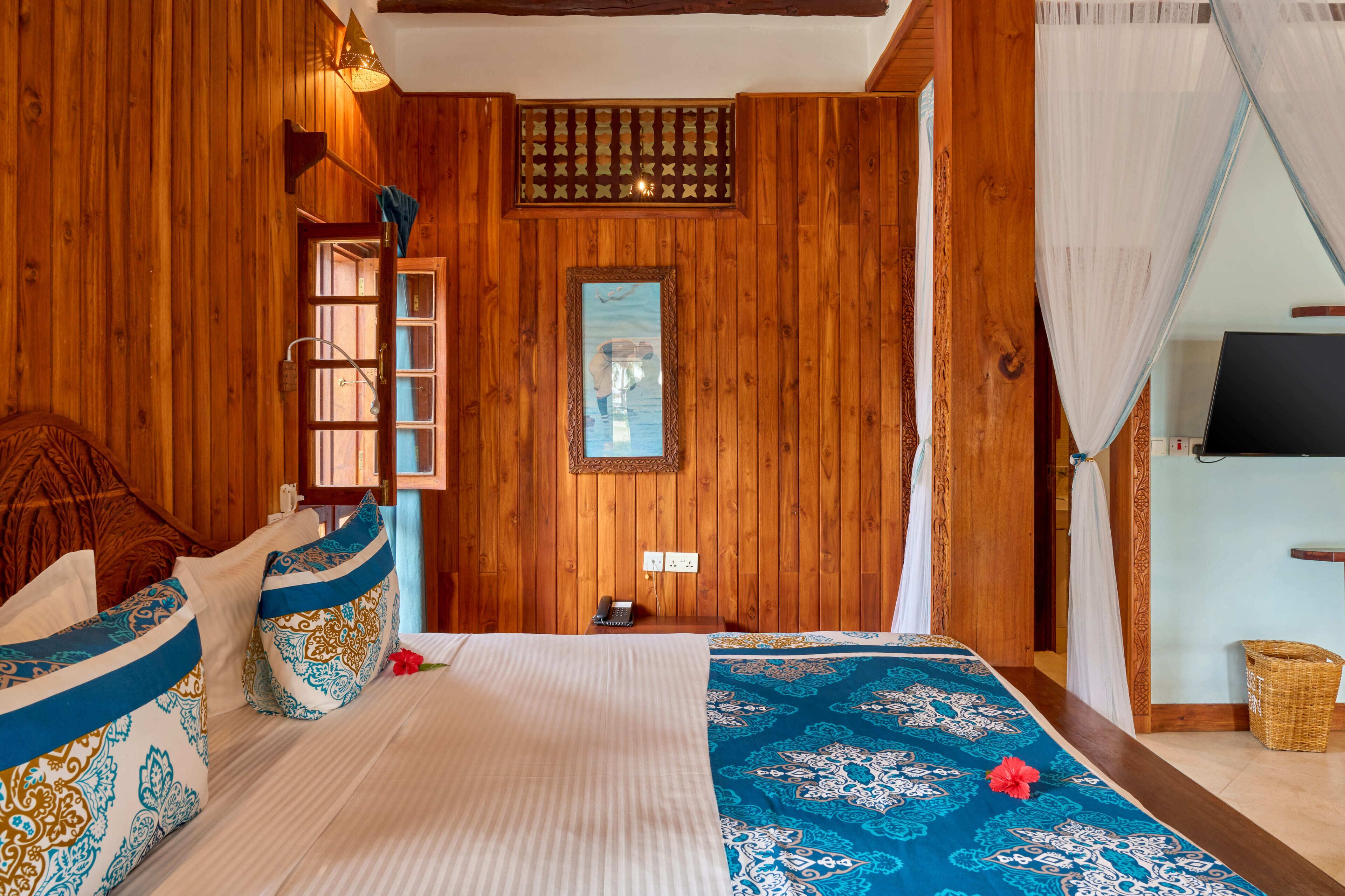 A wooden room with a bed, a wall-mounted TV, a telephone, and a window with a view.