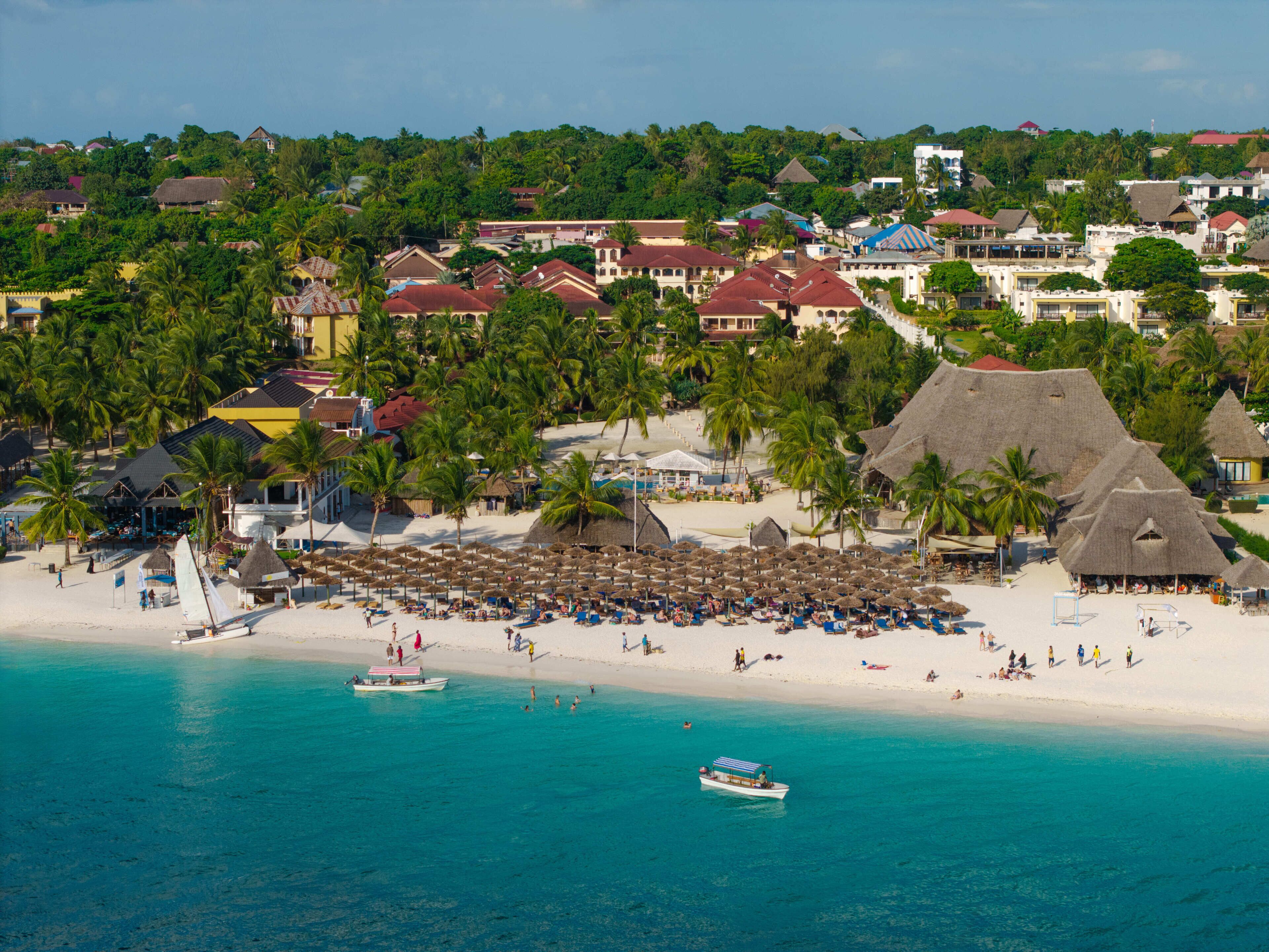 A beach resort with thatched-roof structures, a sandy beach, and clear turquoise waters.