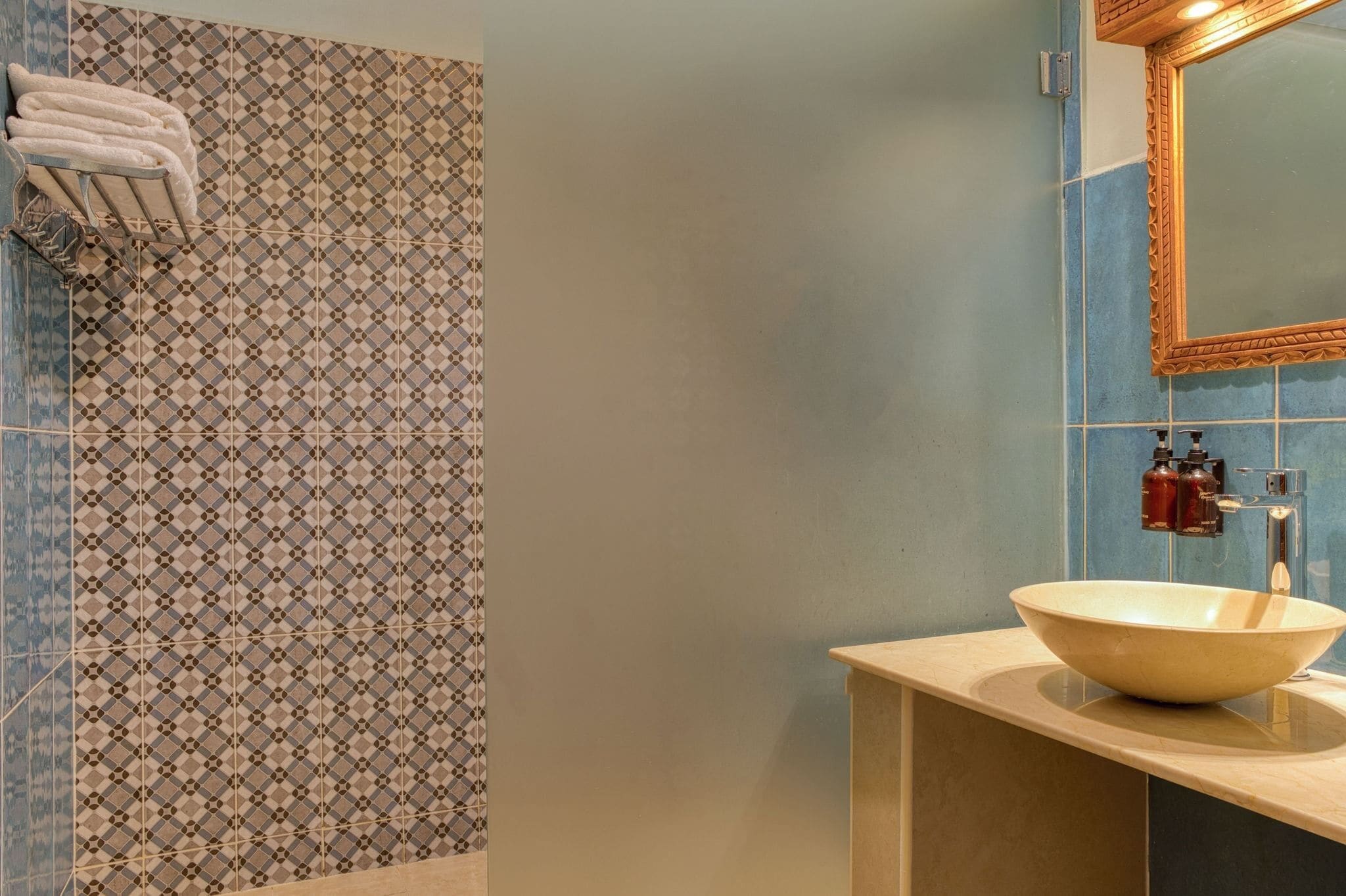Une salle de bain avec un mur recouvert de carreaux à motifs, un lavabo avec un receveur en forme de cuvette et un miroir doté d’un cadre décoratif.
