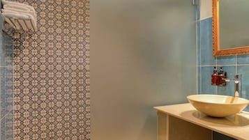A bathroom with a patterned tile wall, a sink with a bowl basin, and a mirror with a decorative frame.