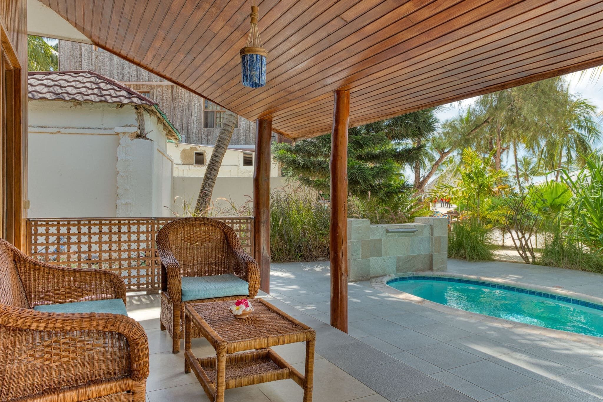 A covered outdoor area with wicker furniture, a pool, and a view of a residential building.