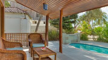A covered outdoor area with wicker furniture, a pool, and a view of a residential building.