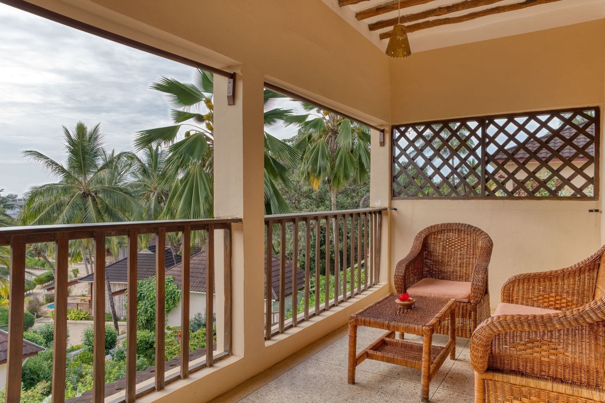 A balcony with wicker furniture, a view of palm trees, and a lattice partition.