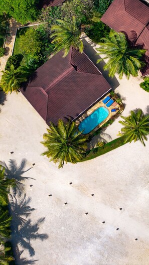 An aerial view of a property with a swimming pool, surrounded by palm trees and a red-roofed building. - Kendwa Rocks Beach Hotel (Kendwa)