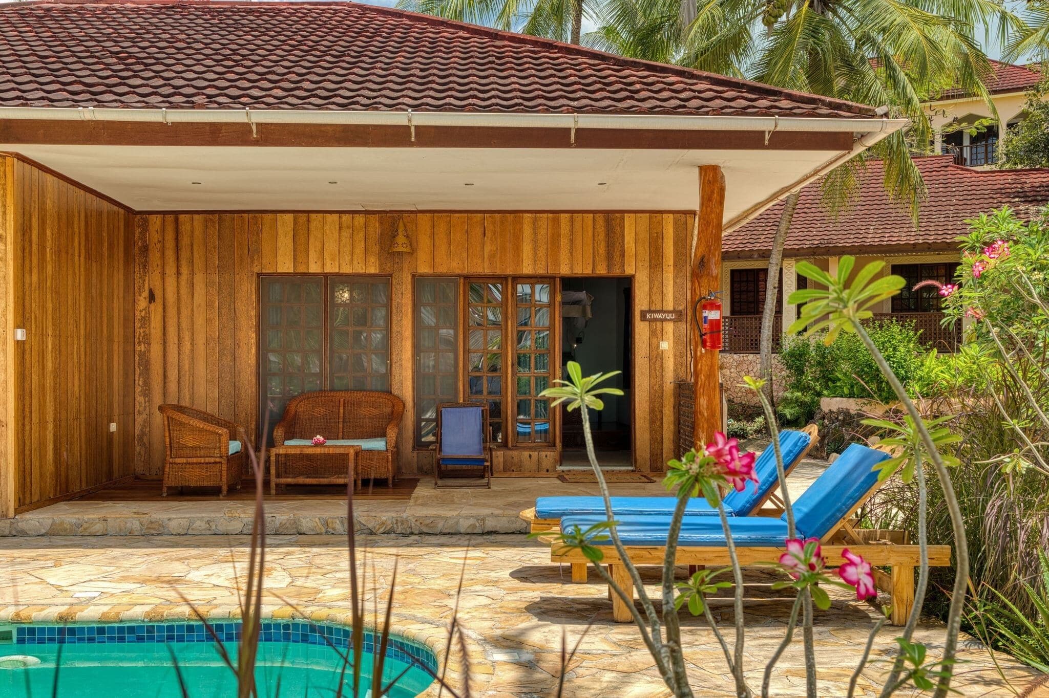 Eine Holzvilla mit Ziegeldach, einem Pool und einer überdachten Terrasse mit Möbeln.