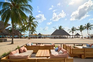 A beachside lounge area with wooden furniture and thatched-roof structures.