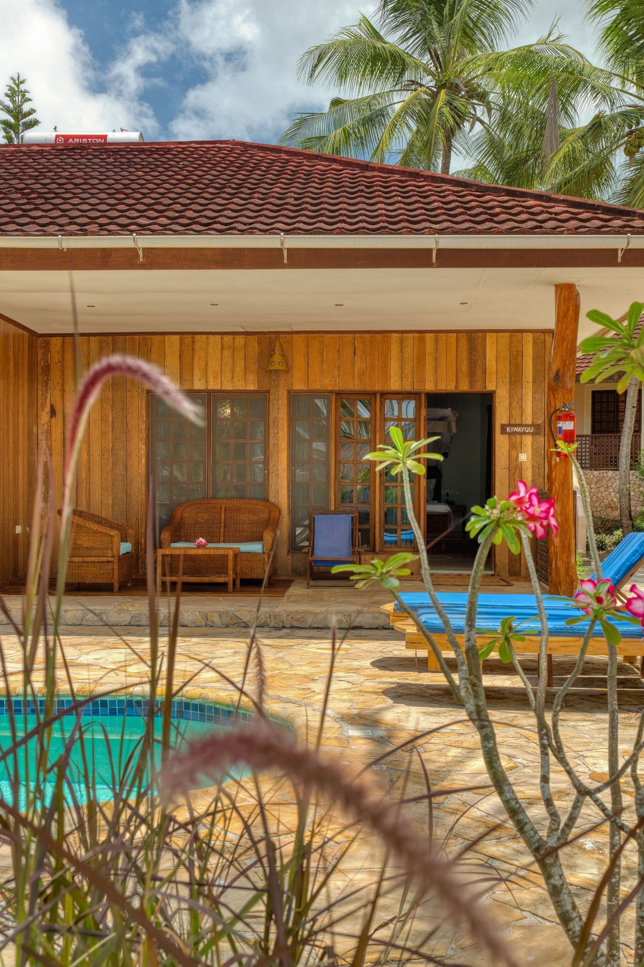 A wooden house with a tiled roof, a pool, and a lounge area with a chair and a table.