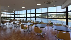 A spacious room with large windows offering a view of the sea and hills. Tables and chairs are arranged for dining or meetings. - Ikijimaso (Iki)